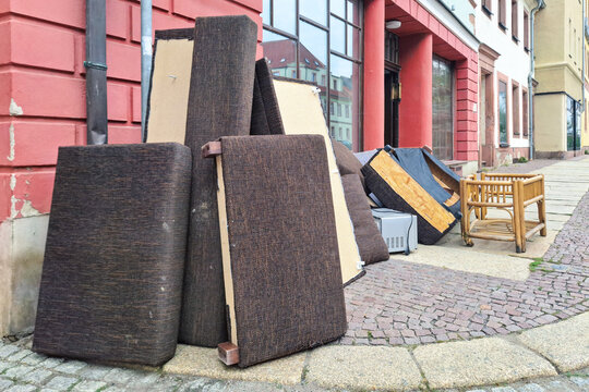 Discarded household items including dismantled couch and bamboo chair abandoned on street, reflecting urban waste and the need for proper furniture disposal. Collection, removal of thrown furniture.
