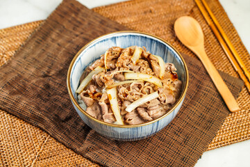 UMAI Beef Donburi with chopsticks and spoon served in bowl isolated on napkin side view of Japanese food