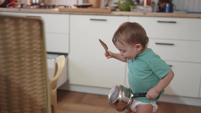 baby plays in the kitchen. happy family kid concept. baby knocks on pots opens kitchen drawers lifestyle plays plays around discovers the world. baby son playing with pots in the kitchen