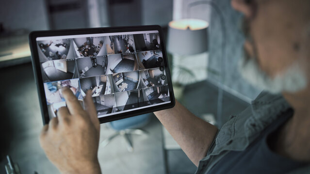 Professional installer watches security cameras in stylish office using tablet computer. View from surveillance cameras displayed on tablet screen. Monitoring and tracking. CCTV system and privacy.