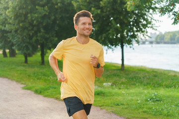 A man in a yellow shirt jogs happily along a park path, surrounded by lush greenery and riverside scenery.