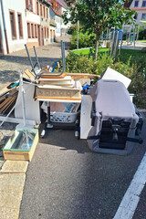 Discarded items including overturned office chair, wooden boards, home furnishings cluttering sidewalk, reflecting urban waste management issues, necessity for responsible disposal. Vertical picture.