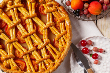 Apricot pie decorated with dough ornament and a metal basket with fruits and berries.