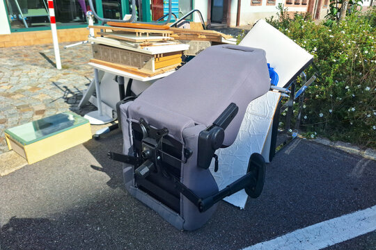 Assorted discarded items including overturned office chair, wooden boards, and home furnishings cluttering sidewalk, reflecting urban waste management issues and necessity for responsible disposal.