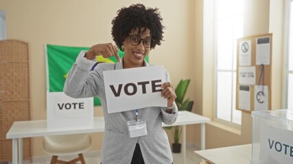 An african american woman with curly hair holds a vote sign and points at a brazilian flag in an indoor electoral college room.