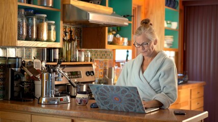 Fototapeta premium Mature woman in bathrobe looks worried and concerned telecommuting from home with her laptop computer.