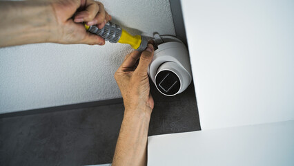 Professional male technician or installer attaches security camera to the ceiling in office building using screwdriver tool. Monitoring and tracking system. CCTV system, video surveillance and privacy