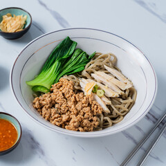 A white bowl of Asian noodles topped with minced pork, sliced chicken breast, and bok choy, served...