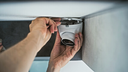 Professional male installer screws CCTV camera to the ceiling in office room using screwdriver tool...