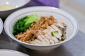 A white bowl filled with Asian noodles, topped with minced pork, sliced chicken, and bok choy, placed on a dark surface, ideal for showcasing traditional Asian cuisine in food photography