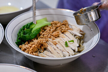 A white bowl filled with Asian noodles, topped with minced pork, sliced chicken, and bok choy, placed on a dark surface, ideal for showcasing traditional Asian cuisine in food photography