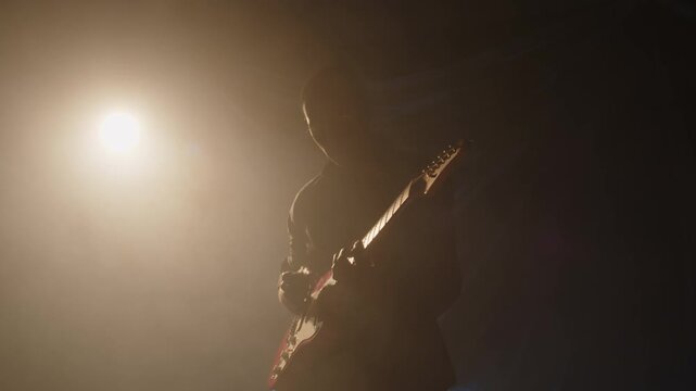 Silhouette of African American guitarist performing solo on foggy stage with backlight