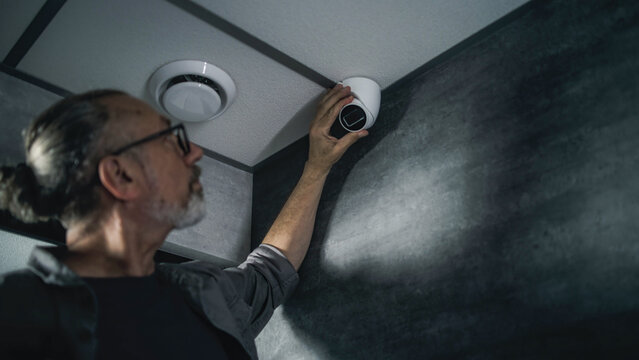 Male mature installer uses tablet computer with professional software to set up surveillance camera in office space, adjusts the angle. Monitoring and tracking. Security and CCTV system. Zoom Out.