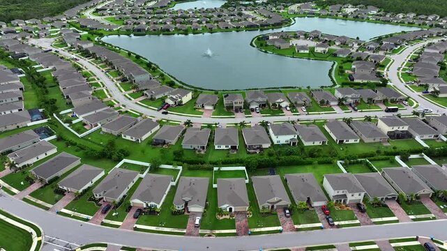 Suburban community with central lake in Florida. Rows of single-family homes with manicured lawns surround the water. Organized residential planning in focus. Aerial.
