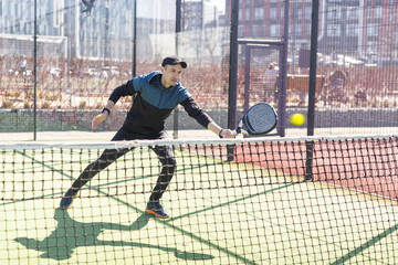 Obraz premium Man playing padel in a green grass padel court indoor behind the net