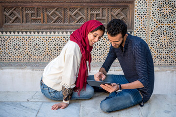 Young Muslim couple in relationship smiling while working on tablet