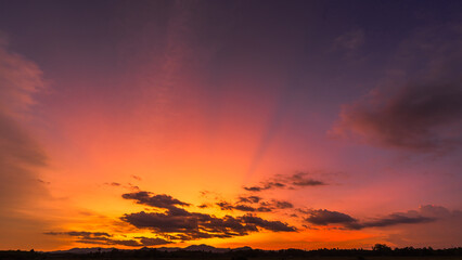 Sunset sky clouds over silhouette hill countryside with orange, yellow sunlight sun rays in the evening on twilight dark blue, Horizon sky landscape, Dusk