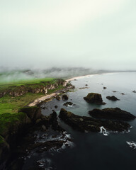 Stimmungsvolle Aufnahme bei bewölktem Himmel von der Küste Nordirlands mit Felsen Klippen Strand und grünen saftigen Wiesen