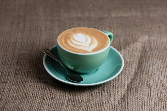 A cup of coffee on a saucer with a spoon stands on a burlap tablecloth