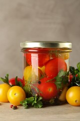 Different pickled tomatoes in jar and fresh ingredients on wooden table, closeup