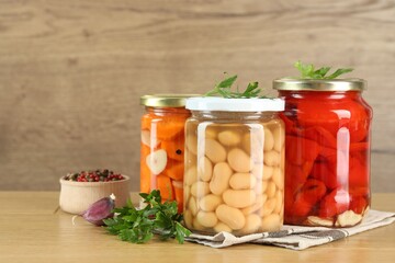 Different pickled products in jars and spices on wooden table