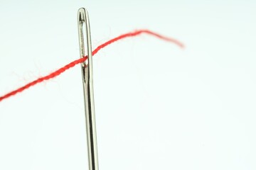 Sewing needle with red thread on white background, closeup