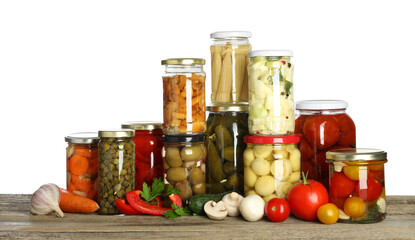 Different pickled products in jars and fresh vegetables on wooden table against white background