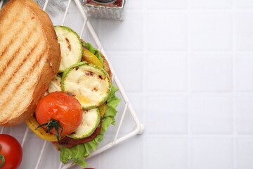 Tasty sandwich with grilled vegetables on white tiled table, flat lay. Space for text