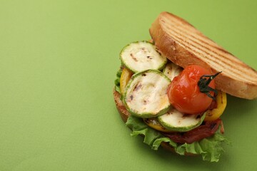 Tasty sandwich with grilled vegetables on green background, closeup. Space for text