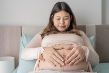 Pregnant asian woman holds hands on belly touching her baby caring about her health Beautiful happy pregnant woman tender mood photo of pregnancy