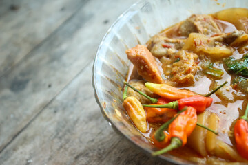Seblak is a typical Indonesian dish with a savory and spicy taste. Made from wet crackers cooked with vegetables, sausage, eggs. a bowl of seblak on a wooden table.