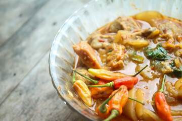 Seblak is a typical Indonesian dish with a savory and spicy taste. Made from wet crackers cooked with vegetables, sausage, eggs. a bowl of seblak on a wooden table.