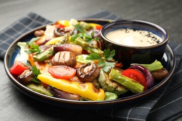 Delicious salad with grilled vegetables and sauce on dark gray textured table, closeup