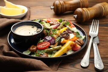 Delicious salad with grilled vegetables and sauce served on wooden table, closeup