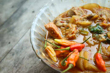 Seblak is a typical Indonesian dish with a savory and spicy taste. Made from wet crackers cooked with vegetables, sausage, eggs. a bowl of seblak on a wooden table.