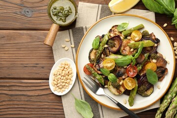 Delicious salad with grilled vegetables, basil, pesto sauce, pine nuts and fork on wooden table, flat lay. Space for text