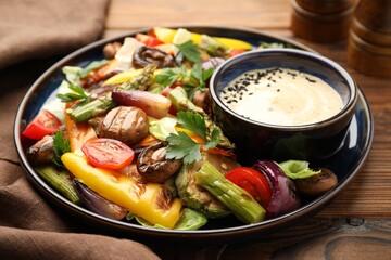 Delicious salad with grilled vegetables and sauce on wooden table, closeup