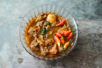 Seblak is a typical Indonesian dish with a savory and spicy taste. Made from wet crackers cooked with vegetables, sausage, eggs. a bowl of seblak on a wooden table.