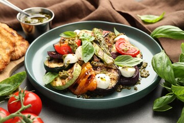 Delicious salad with grilled vegetables, pesto sauce and basil on gray table, closeup