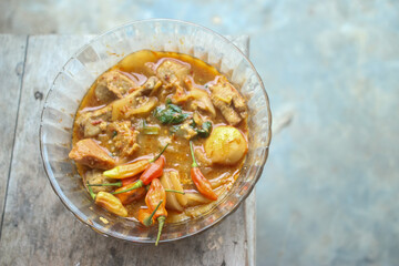 Seblak is a typical Indonesian dish with a savory and spicy taste. Made from wet crackers cooked with vegetables, sausage, eggs. a bowl of seblak on a wooden table.