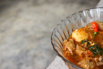 Seblak is a typical Indonesian dish with a savory and spicy taste. Made from wet crackers cooked with vegetables, sausage, eggs. a bowl of seblak on a wooden table.