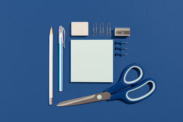 Empty blue paper sheet with pen, pencil, pins, scissors and clips on a blue background. Office and...
