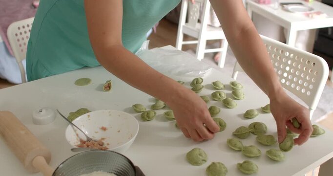 A person expertly making green dumplings on a table, showcasing culinary skills and fresh ingredients. Make even rows with your hands for packing and storing dumplings.