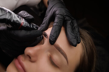 Close-up of the master stretching the eyebrow with two fingers thus applying permanent makeup with...