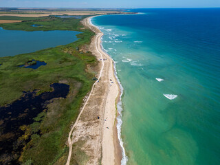 Aerial view of a sandy beach with scattered tents and umbrellas along the shoreline. Waves gently wash onto the shore, capturing a peaceful and relaxing summer day by the ocean
