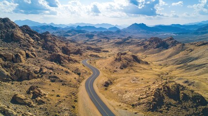 Aerial perspective of a curving road amidst rocky mountains, with wide areas of barren land for text placement.