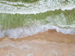 Aerial view of ocean waves crashing onto a sandy beach, creating a beautiful contrast between the emerald green water and the warm, textured sand. A perfect capture of coastal beauty
