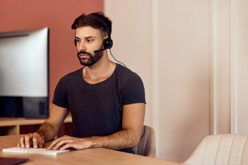 A busy man working over the computer, at the office, wearing headphones, looking focused.