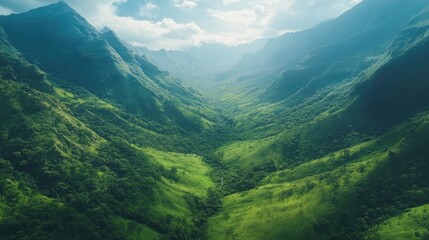 Obraz premium Overhead shot of a lush green valley nestled between mountain ridges with plenty of copy space in the sky