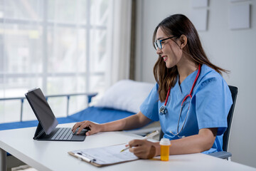 Smiling young nurse working on medical report and using digital tablet in hospital room